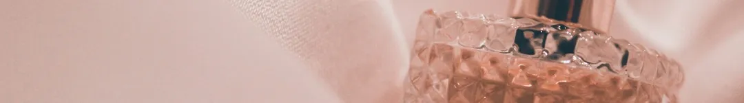 A close-up of an elegant perfume bottle with intricate detailing, set against a soft, blush-pink fabric backdrop.